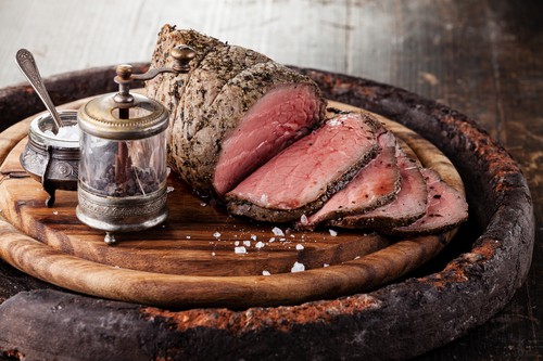 Roast beef on cutting board with saltcellar and pepper mill