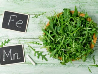 Fresh green arugula in bowl on wooden table