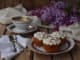 Romantic composition of  bouquet white and purple lilacs, cupcakes with curd cream, cups coffee on wooden background.