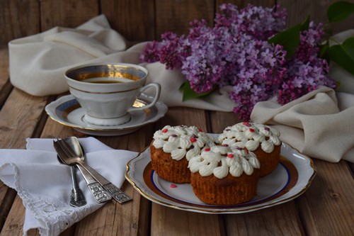 Romantic composition of  bouquet white and purple lilacs, cupcakes with curd cream, cups coffee on wooden background.